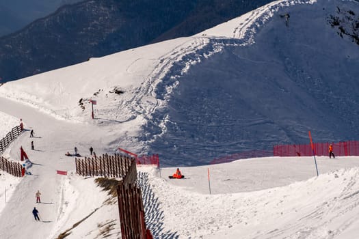 Skiers and snowboarders enjoy a snowy mountain slope. Wooden fences and red safety nets line the groomed runs. A scenic, high-altitude winter vista.