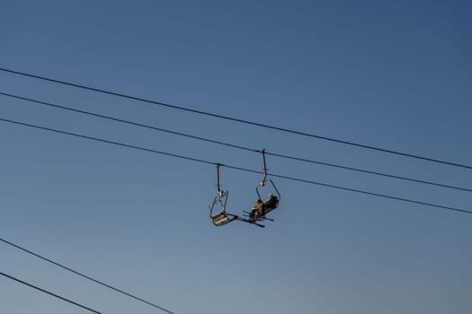 Two people ride a chairlift against a clear twilight sky. Empty chairlift visible. Multiple cables support the lift.