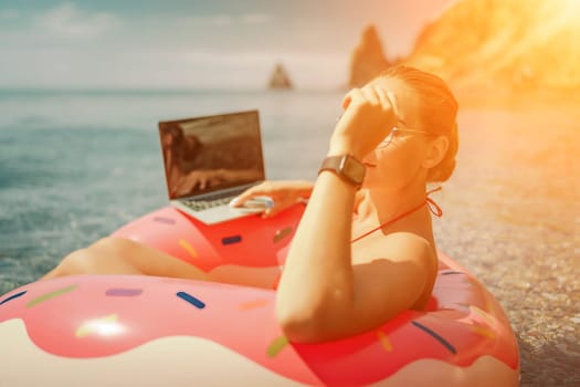 Woman laptop sea. Freelancer woman in sunglases floating on an inflatable big pink donut with a laptop in the sea. People summer vacation rest lifestyle concept
