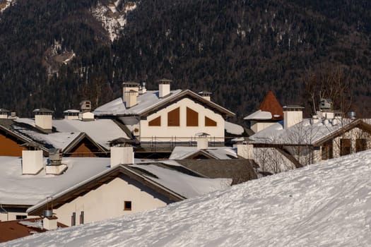 Snow-covered chalet rooftops and chimneys against a mountainous backdrop. Winter scene.
