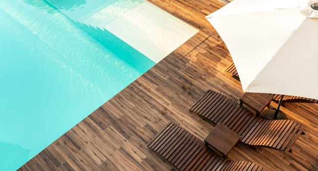 Turquoise swimming pool with wooden deck, lounge chairs, and umbrella in a modern outdoor setting