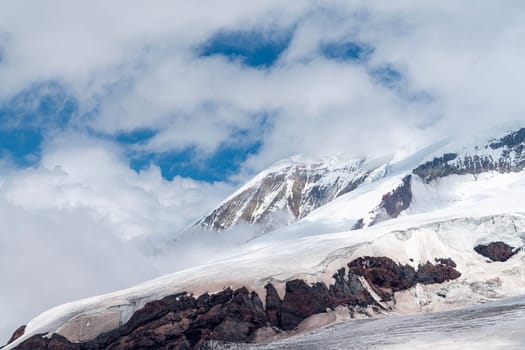 Majestic mountain peak is visible in the backdrop, partially covered by clouds. Snow and rocky terrain create contrast, highlighting the beauty and grandeur of nature in the scene.
