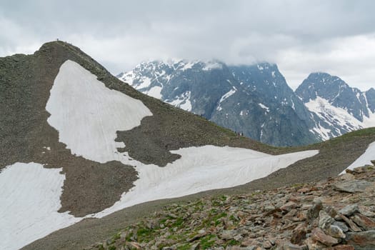Snow-covered slopes meet rugged mountains under a cloudy sky. The scene showcases a stunning blend of natural elements, capturing the beauty of alpine terrain in an untouched wilderness.