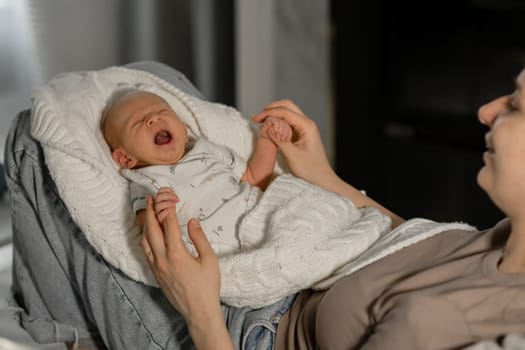 A mother is holding her yawning baby close, enjoying a tender moment while relaxing in a cozy indoor setting during the evening hours.