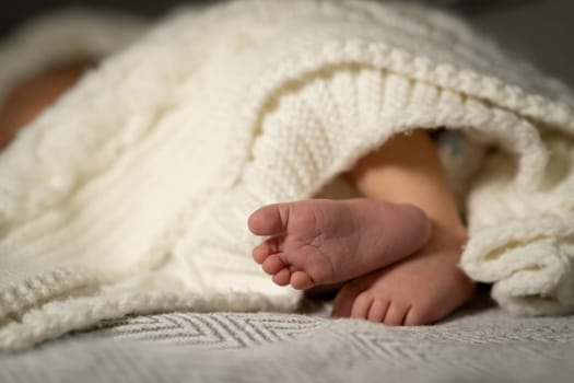 Soft baby feet are visible as the little one relaxes under a warm knitted blanket in a peaceful home setting during the afternoon.