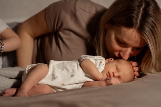A loving mother kisses her peacefully sleeping baby on the bed, creating an intimate atmosphere filled with warmth and affection during a relaxing afternoon.