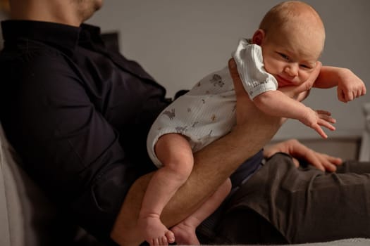 A baby joyfully stretches and plays with their parents leg while enjoying a warm and cozy indoor atmosphere on a couch in the evening.