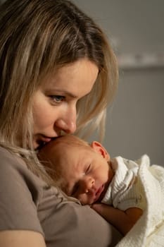 A mother gently kisses her newborn as they enjoy a peaceful moment together in a warm, intimate indoor environment, highlighting their bond.