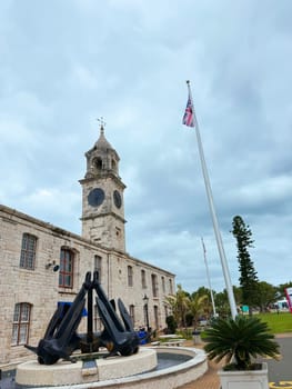 Bermuda, USA, Royal Naval Dockyard November 22. 2023 Clocktower Mall, featuring large maritime anchor sculpture, stone architecture, and British flag under cloudy sky.