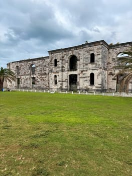 Old stone ruins of a military-era building located in the Royal Naval Dockyard, Bermuda, under overcast skies and surrounded by grass.