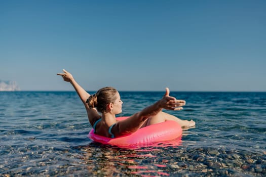 A woman is floating on a pink inflatable raft in the ocean. She is smiling and she is enjoying herself