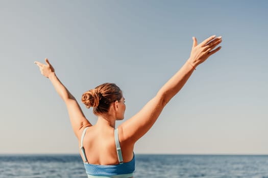 A woman is standing on the beach with her arms raised in the air. The sky is blue and the ocean is calm. The woman is happy and enjoying the beautiful day