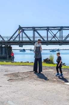 Tauranga New Zealand - March 22 2025; street art and perfromance on city streets, Eric "the tall artist" with boy and harbour bridge in background .