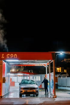 Service worker at a car wash washes a car with a hose. Back view. High quality photo