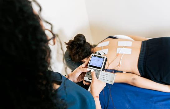 View of physiotherapist electrostimulating a patient. Lower back therapy with electrode pads. Electrode treatment to patient lying down, Professional physiotherapist electrostimulating patient