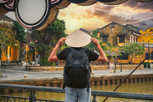 back of male tourist in a Vietnamese hat on a bridge in old town in Hoi An in Vietnam in Asia