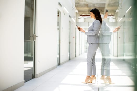 Pretty young business woman using mobile phone in the office hallway