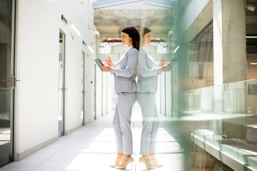 Pretty young business woman using mobile phone in the office hallway