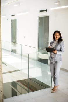 Pretty young business woman using mobile phone in the office hallway