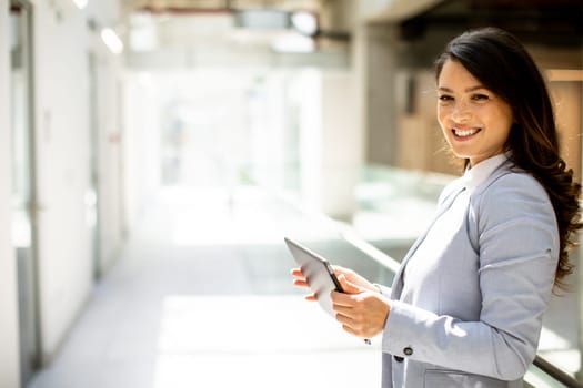 Pretty young woman working on digital tablet in the office hallway