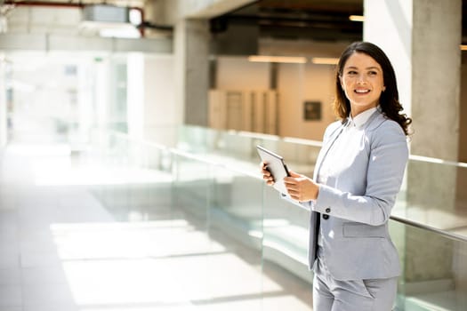 Pretty young woman working on digital tablet in the office hallway