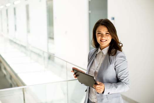 Pretty young woman working on digital tablet in the office hallway