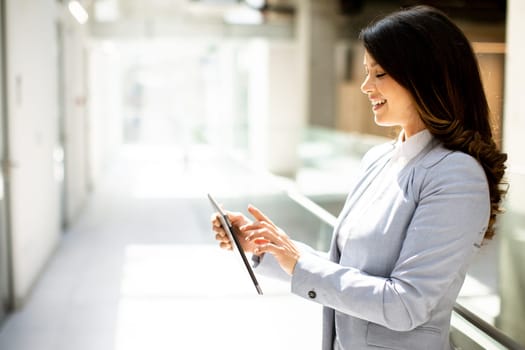 Pretty young woman working on digital tablet in the office hallway