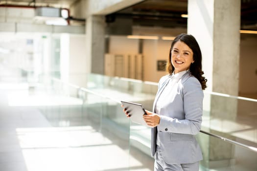 Pretty young woman working on digital tablet in the office hallway