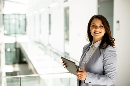 Pretty young woman working on digital tablet in the office hallway