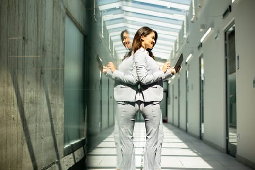 Pretty young woman working on digital tablet in the office hallway