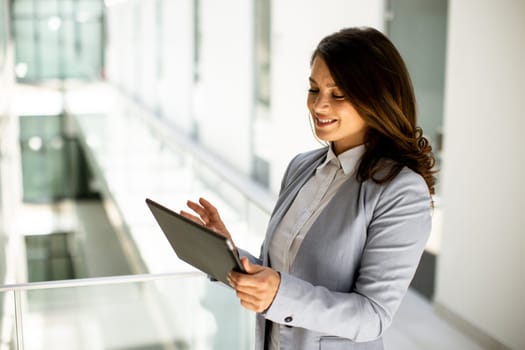 Pretty young woman working on digital tablet in the office hallway