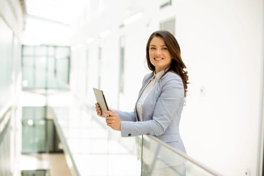 Pretty young woman working on digital tablet in the office hallway