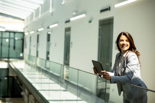Pretty young woman working on digital tablet in the office hallway