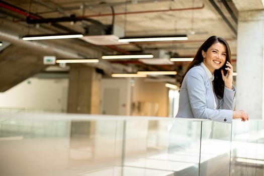 Pretty young business woman using mobile phone in the office hallway