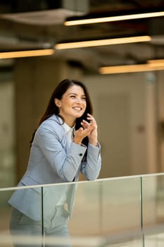 Pretty young business woman using mobile phone in the office hallway