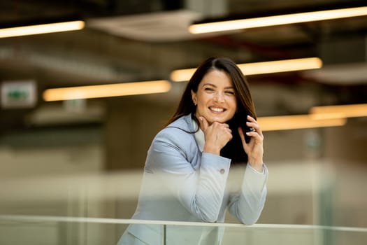 Pretty young business woman using mobile phone in the office hallway