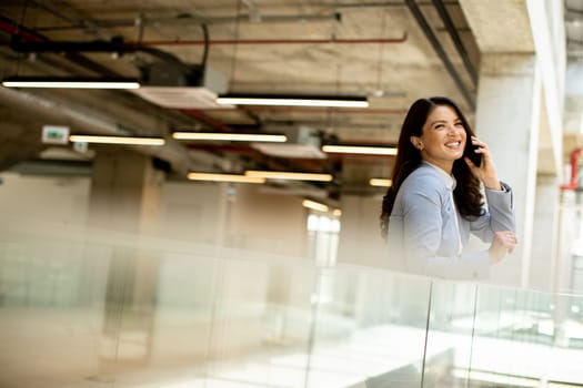 Pretty young business woman using mobile phone in the office hallway