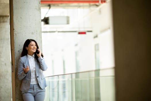 Pretty young business woman using mobile phone in the office hallway