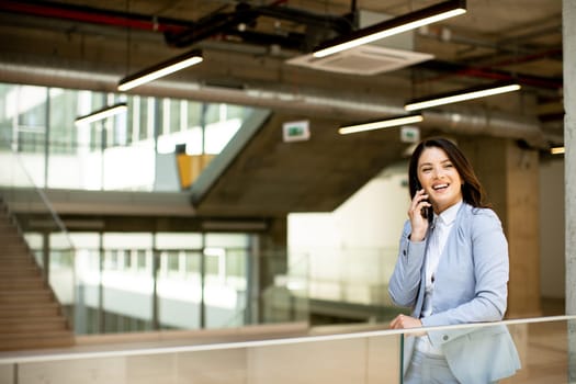Pretty young business woman using mobile phone in the office hallway