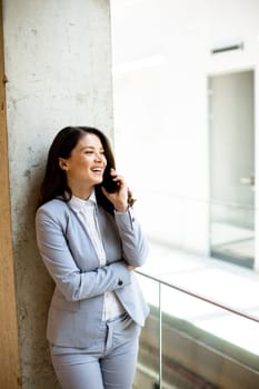 Pretty young business woman using mobile phone in the office hallway