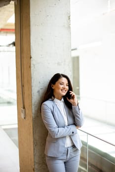 Pretty young business woman using mobile phone in the office hallway