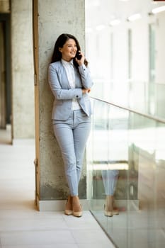 Pretty young business woman using mobile phone in the office hallway