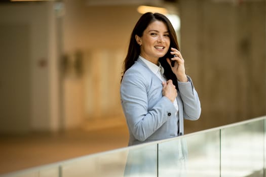 Pretty young business woman using mobile phone in the office hallway