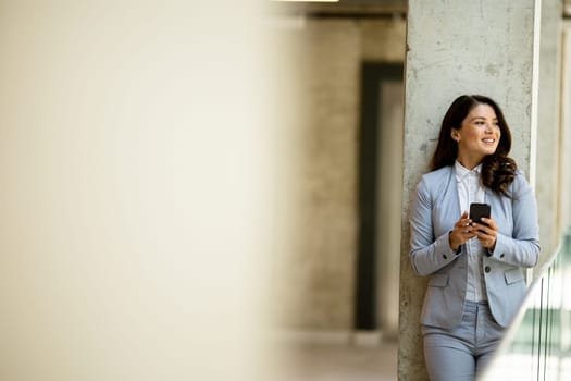 Pretty young business woman using mobile phone in the office hallway