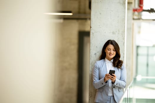 Pretty young business woman using mobile phone in the office hallway