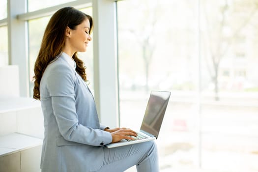 Pretty young business woman sitting on the stairs on office hallway and working on laptop