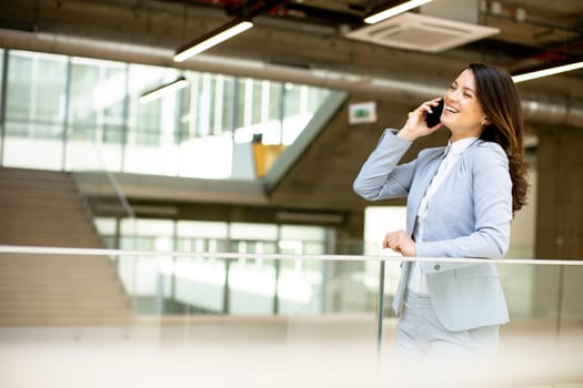 Pretty young business woman using mobile phone in the office hallway