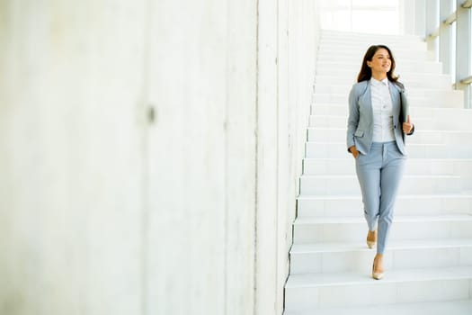 Young business woman walking down the stairs and holding laptop at the office hallway