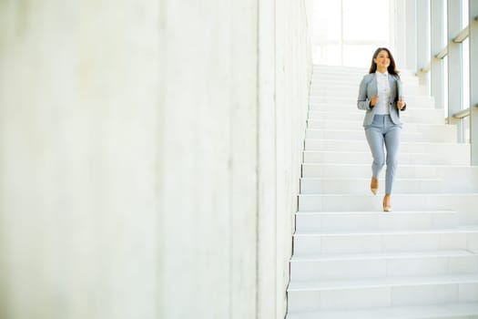 Young business woman walking down the stairs and holding laptop at the office hallway