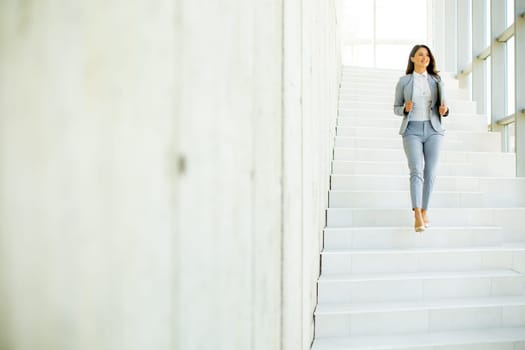 Young business woman walking down the stairs and holding laptop at the office hallway